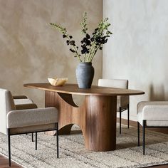 a vase with flowers on top of a wooden table next to two chairs and a rug