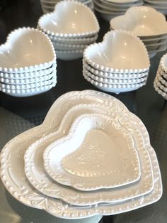 white heart shaped dishes are stacked on a black tablecloth with other plates and bowls in the background