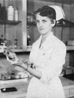 an old black and white photo of a woman holding a bottle in her hand while standing in a kitchen