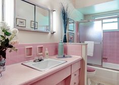 a bathroom with pink tiles and white flowers in the vase on the sink next to the bathtub