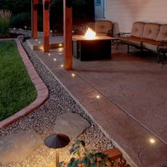 a fire pit in the middle of a patio with seating and lights on it's sides