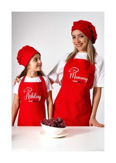 two women in red aprons and hats standing next to a bowl of grapes on a table