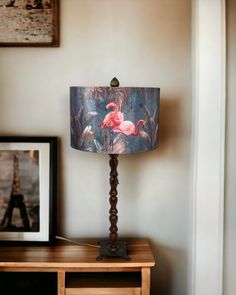 a lamp with a pink flamingo print on it sitting on a table next to a framed photograph