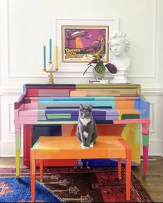 a cat sitting on top of a colorful bench in front of a painting and candles