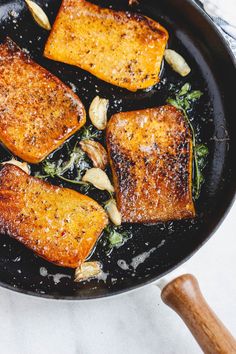 three pieces of fish cooking in a skillet with broccoli and nuts on the side