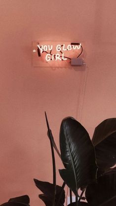 a neon sign that says you glow girl on the side of a wall next to a potted plant