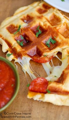 two pieces of waffles with cheese and strawberries on them next to a bowl of ketchup