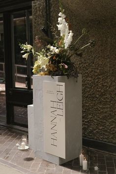 a large white vase with flowers in it sitting on the sidewalk next to a building