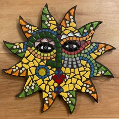 a sun face made out of stained glass on a wooden surface with dots and circles around it