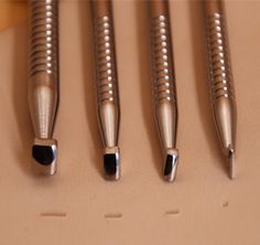 four metal pens are lined up in a row on a surface with holes and rivets