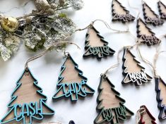 wooden christmas trees are hanging from twine strings on a table with snow and evergreen branches