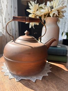 a tea pot with a wooden handle sitting on top of a table next to flowers