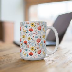 a coffee mug sitting on top of a wooden table next to a laptop computer in the background