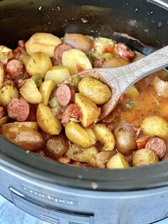 a wooden spoon in a slow cooker filled with potatoes and sausage