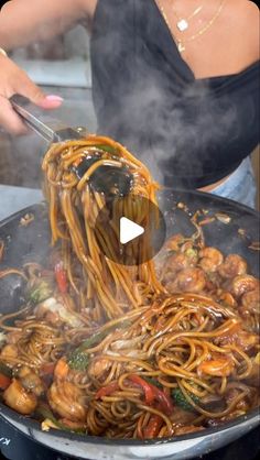 a woman stirs noodles with chopsticks in a wok