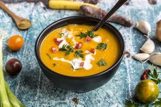 a black bowl filled with carrot soup surrounded by vegetables and other ingredients on a blue surface