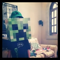 a person in a minecraft creeper costume standing next to a couch with a box on it's head