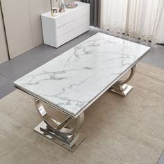 a white marble table sitting on top of a rug in front of a dresser and window