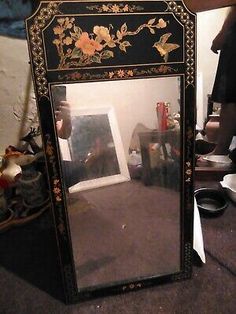 an ornate black and gold mirror with flowers on the front, sitting in a room