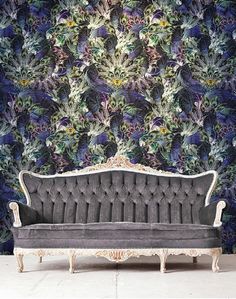 an old couch sitting in front of a wall covered with purple and green flowers on it