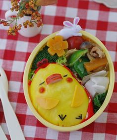 a yellow bowl filled with food on top of a red and white checkered table cloth