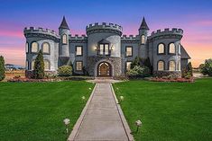 a large castle like building sitting in the middle of a lush green field at sunset