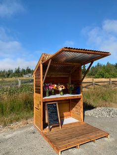 a wooden stand with flowers on it in the middle of some grass and dirt area