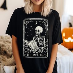 Presenting our The Reader Tarot Card graphic tee! This unique and original design is perfect for both adults and youth. Tees are unisex regular fit, in soft combed-cotton fabric. For an oversized look, please consider sizing up.  Premium Quality: Crafted with love and attention to detail, our graphic tees are made using ultra soft and comfortable cotton based tees, ensuring a cozy fit for all-day wear. Our professional printing process guarantees vibrant colors that won't fade, allowing you to enjoy this charming design for many years to come. Handmade with Love: Each tee is individually crafted in our own printing studio to ensure a professional and high quality print. Oversized Skull Print T-shirt For Fall, Tarot Card Shirt Design, Tarot Card Shirts, The Reader Tarot Card, Tarot Card Skeleton, Tarot Card Shirt Tees, Printing Studio, Witchy Halloween T-shirt With Graphic Print, Floral Graphic