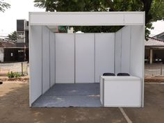 a white portable toilet sitting in a parking lot next to a tree and fenced area