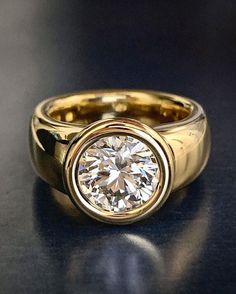 a yellow gold ring with a round diamond in the center on a black table top