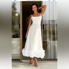 a woman standing in front of a door wearing a white dress with ruffles