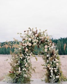 an arch made out of flowers and greenery in the middle of a grassy field