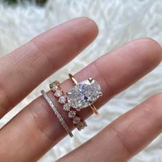 a woman's hand with two rings on top of her finger and the ring has an oval shaped diamond surrounded by smaller round diamonds