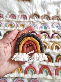 a hand holding a pair of earrings with tassels in front of a rainbow background