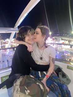 two women are hugging each other while sitting on the edge of a boat at night