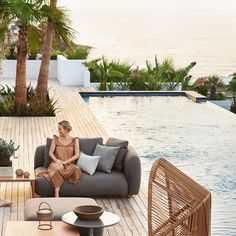 a woman sitting on a couch in front of a pool with palm trees and chairs