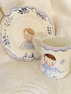 two children's plates and a cup on a white bed with blue trimmings