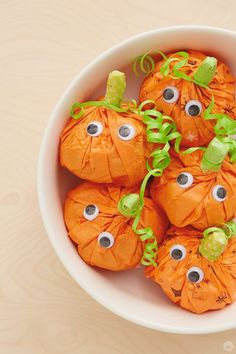 a white bowl filled with orange candy covered in googly eyes and green ribbons on top of a wooden table