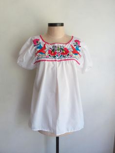 New, never worn. Hand embroidered Mexican peasant blouse. Beautiful, bold traditional floral pattern, hand embroidered with silk thread. Puff sleeves with elastic hem. Measurements laying flat: 16.75" across shoulders 19.5" underarm to underarm 23" across hem 5.5" sleeve length 28" length, from top of shoulder to hem White Bishop Sleeve Tops With Floral Embroidery, White Tops With Floral Embroidery And Bishop Sleeves, Summer Floral Embroidery Blouse With Bishop Sleeves, Summer Blouse With Floral Embroidery And Bishop Sleeves, Cotton Embroidered Puff Sleeve Blouse, Fitted Blouse With Floral Embroidery And Bishop Sleeves, Fitted Bishop Sleeve Blouse With Floral Embroidery, White Blouse With Embroidered Bishop Sleeves, White Embroidered Blouse With Bishop Sleeves