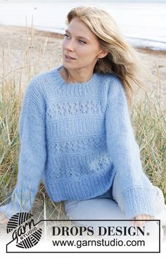 a woman sitting on the beach wearing a blue sweater