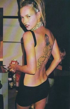 a woman with tattoos on her back holding a drink