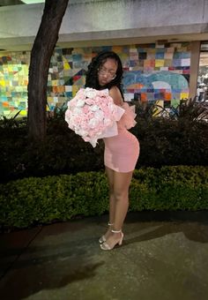 a woman in a short pink dress holding a bouquet of flowers and posing for the camera