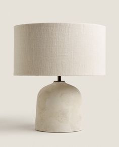 a white table lamp with a beige shade on the base and a light bulb attached to it