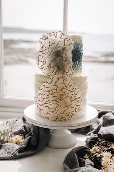 a three tiered cake sitting on top of a white table next to a window