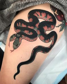 a black and red snake tattoo on the right thigh, with an apple in the background