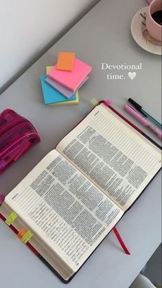 an open book sitting on top of a table next to a pink cup and pen