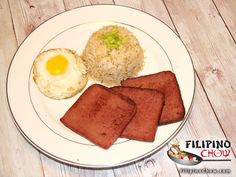 a white plate topped with meat, rice and an egg sitting on top of a wooden table