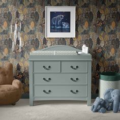 a baby's room with an elephant wallpaper and blue dresser in the foreground