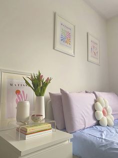 a bed with pink and white pillows on top of it next to two vases filled with flowers