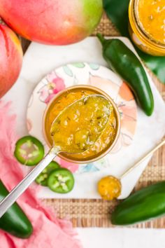 a spoon full of sauce sitting on top of a plate next to green peppers and pomegranates